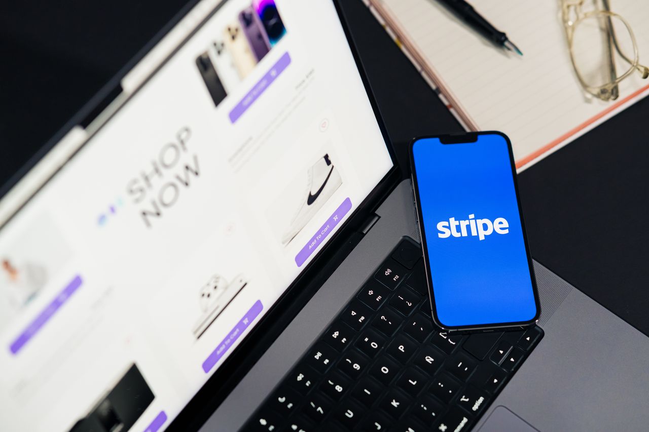 services-03 Un téléphone mobile affichant l’application Stripe sur un ordinateur portable avec un site eCommerce ouvert, illustrant les achats en ligne.